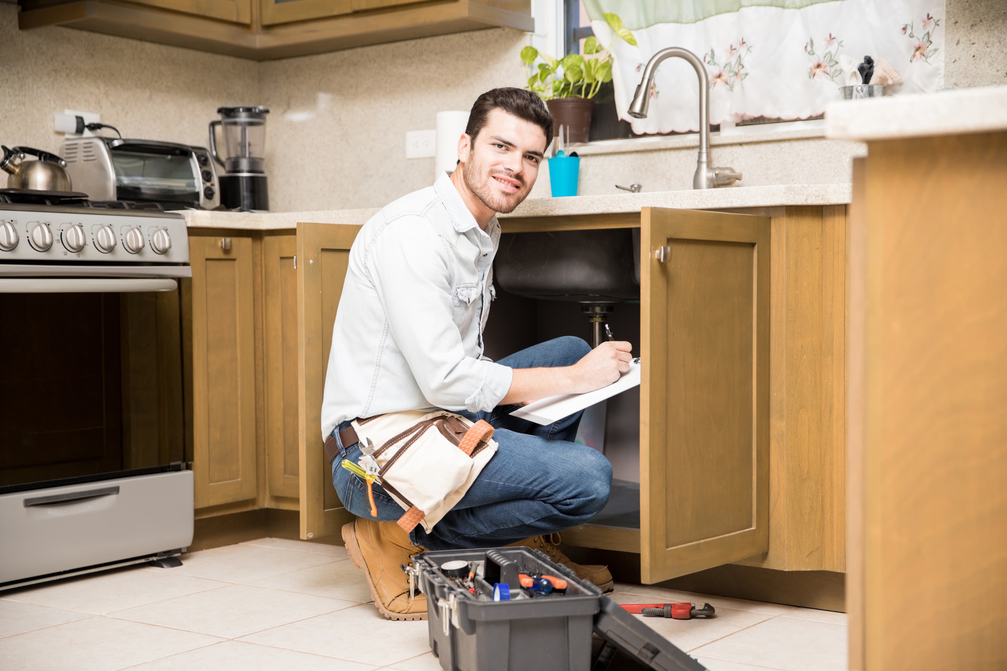 A handyman inspecting plumbing under a kitchen sink